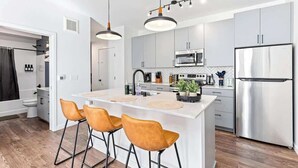 A modern kitchen with a central island, bar stools, stainless steel appliances, and a white color scheme. - 1 Bed Apt + Rooftop | Lake of Isles (Minneapolis)