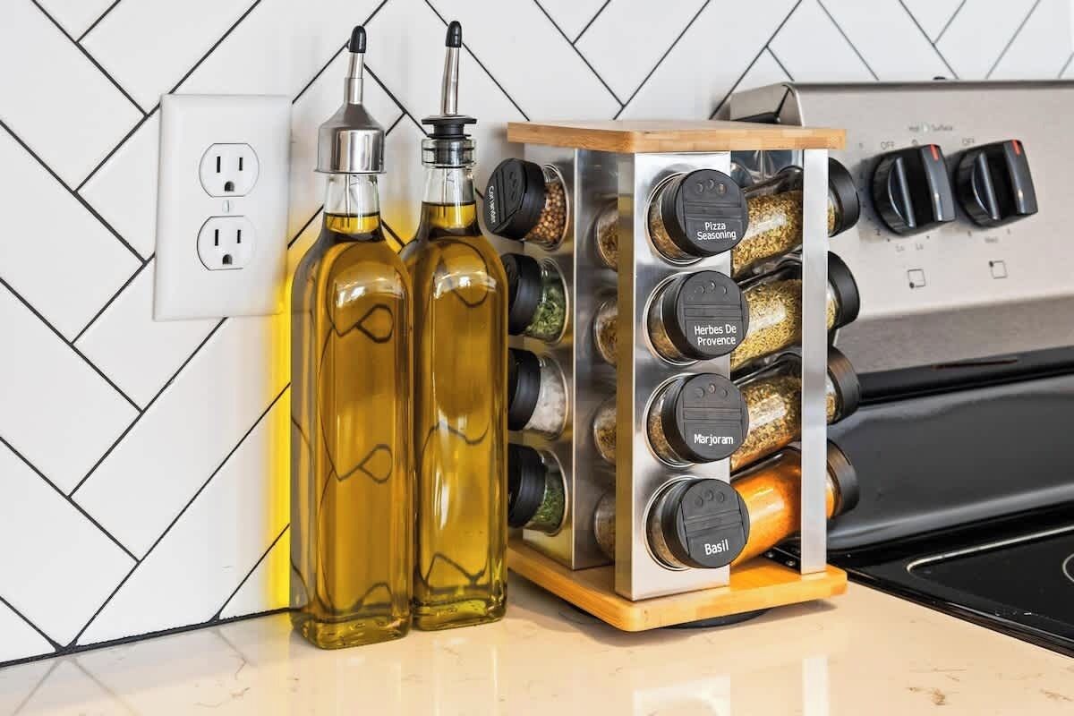 A kitchen with a spice rack holding jars labeled with herbs and spices, and two bottles of oil on the counter.