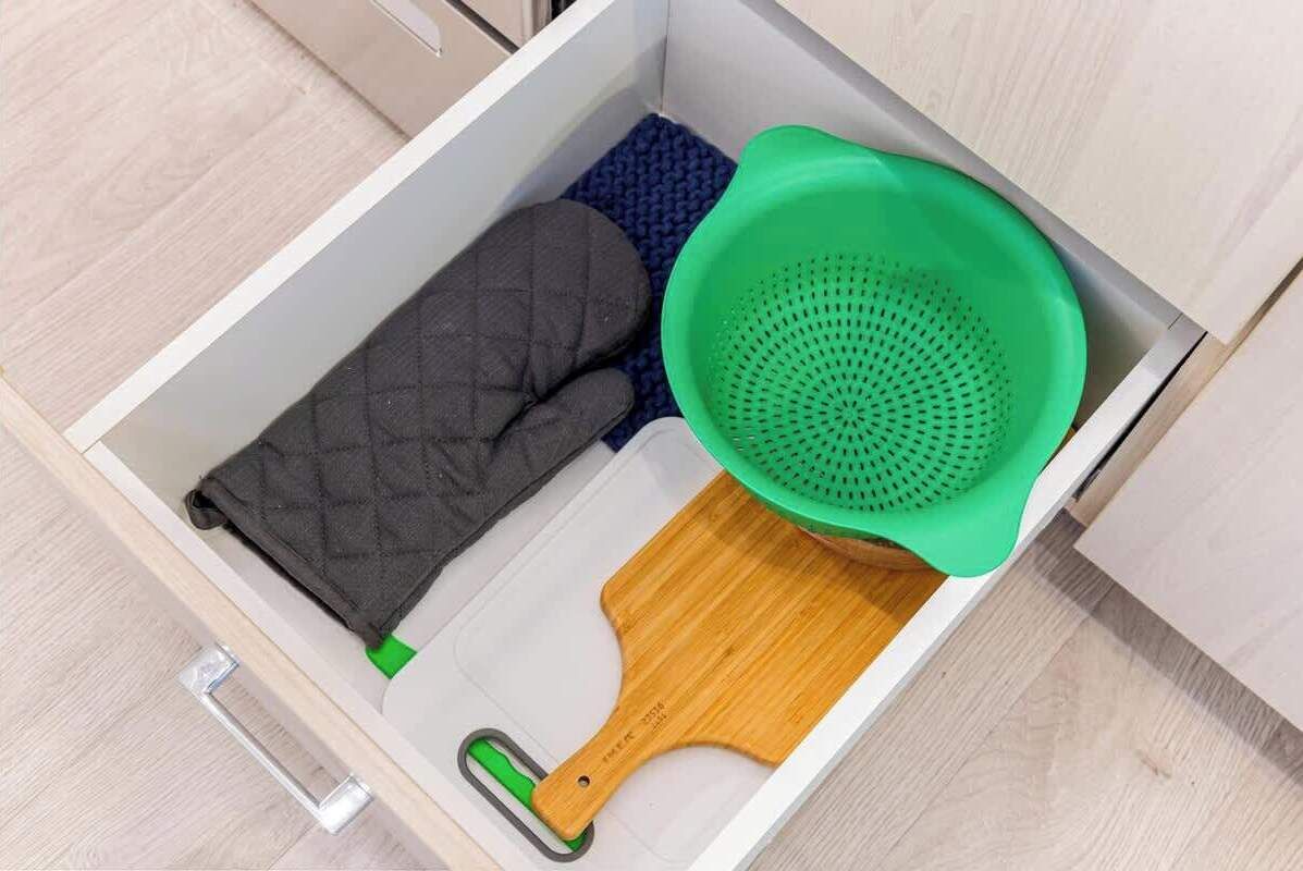 A drawer containing a quilted fabric item, a green colander, and a wooden spatula.