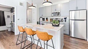 A modern kitchen with white cabinetry, a central island with bar stools, stainless steel appliances, and pendant lighting. - 1Bed Apt, Gym | Lowry Hill | Theater (Minneapolis)