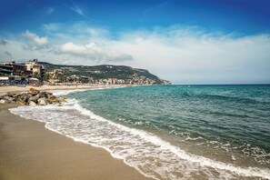 A beach with a rocky shoreline, a clear sky, and buildings in the background. - Holiday apartment with pool and air conditioning (Pietra Ligure)
