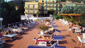 Un espace piscine aménagé sur le toit, avec des chaises longues et des parasols, entouré d’immeubles et de verdure.