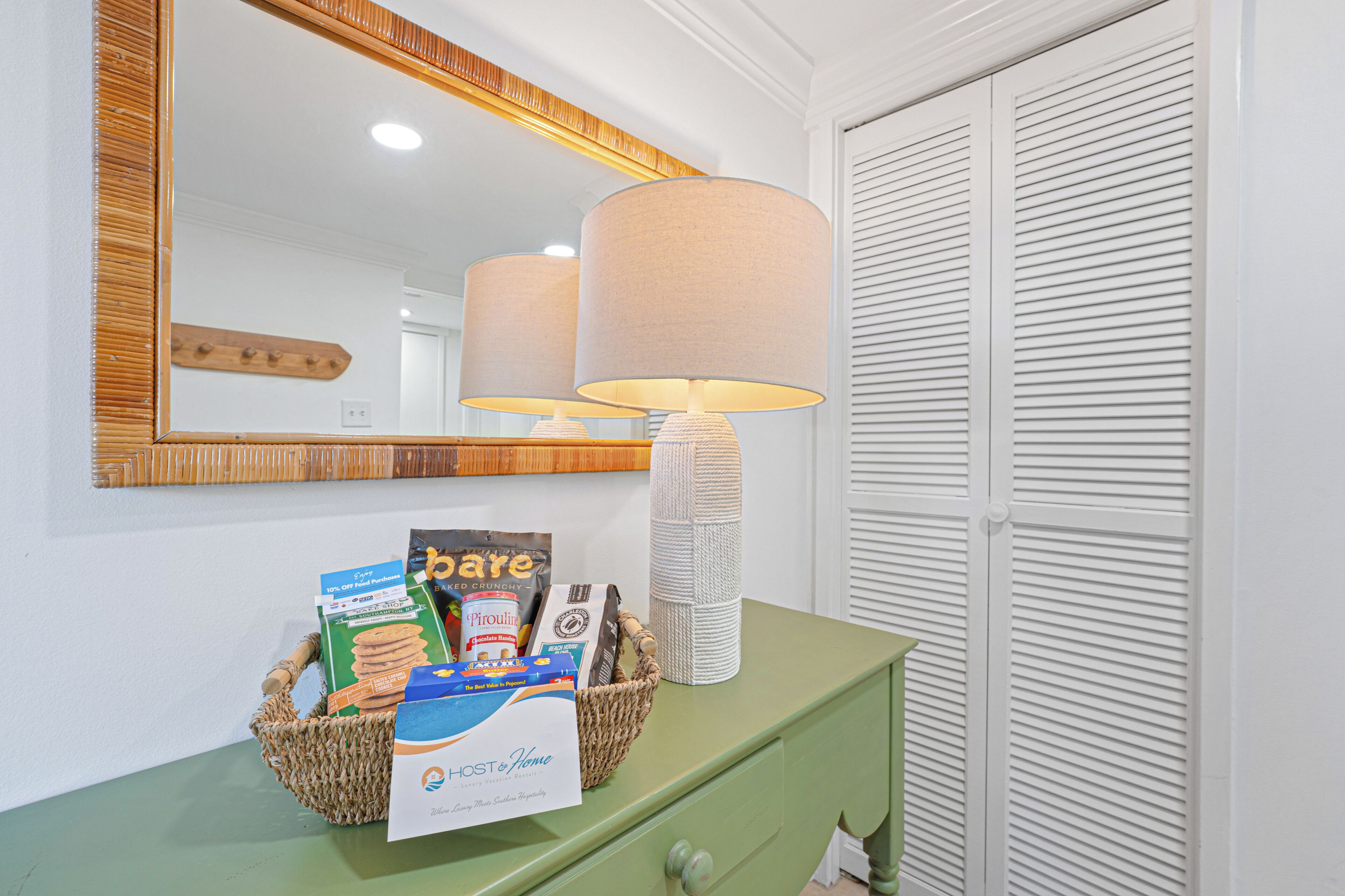 A green dresser with a mirror above it, a lamp, and a basket containing various items including a box of cereal and a bag of chips.