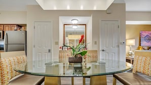 A modern dining area with a glass table, cushioned chairs, and a decorative plant centerpiece. - 7 mins to Disney | 2BR Resort Condo on the Lake (Orlando)