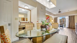 A modern hotel room with a glass dining table, comfortable seating, a ceiling fan, and a view of the cityscape. - 7 mins to Disney | 2BR Resort Condo on the Lake (Orlando)