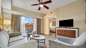 A hotel room with a sofa, armchair, small table, ceiling fan, TV, and a view of the outside. - 7 mins to Disney | 2BR Resort Condo on the Lake (Orlando)