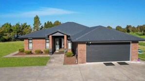 A single-story house with a dark roof, a garage, and a front yard with a lawn and small shrubs.