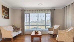 A spacious living room with a wooden floor, two sofas, a coffee table, and a large window with curtains.