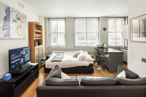 A modern hotel room with a large bed, a sofa, a TV, a kitchen area, and a bookshelf. - Drury Lane - A Slice of Heaven (London)