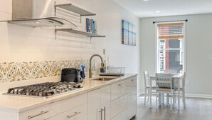 Une cuisine moderne avec des meubles blancs, une cuisinière à gaz et un évier. On y trouve également un coin repas avec une table et des chaises.