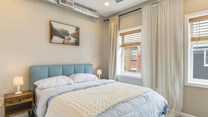 Une chambre à coucher avec un lit, des tables de chevet, un tableau et une fenêtre avec des rideaux.