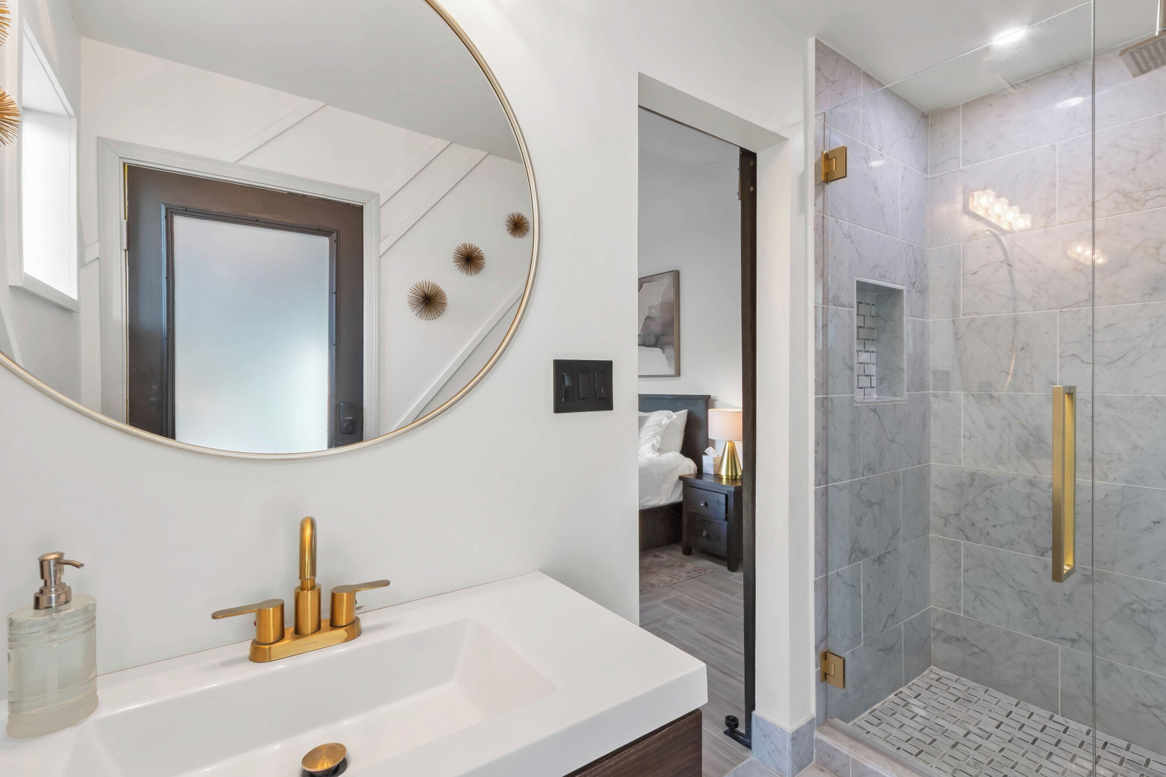 A modern bathroom with a large mirror, a white sink with gold fixtures, and a glass-enclosed shower area.