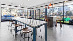 Un espace bar moderne avec une longue table et des tabourets, de grandes fenêtres offrant une vue sur la rue et les bâtiments environnants.