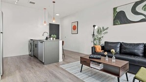 Une cuisine moderne avec un îlot central, un coin repas avec une table basse et un salon doté d’un canapé en cuir noir.