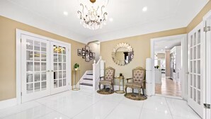 Un vestíbulo amplio con candelabro, una escalera y una zona de comedor con dos sillas.