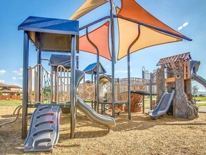 A playground with slides and climbing structures, surrounded by a fence and covered by a canopy.