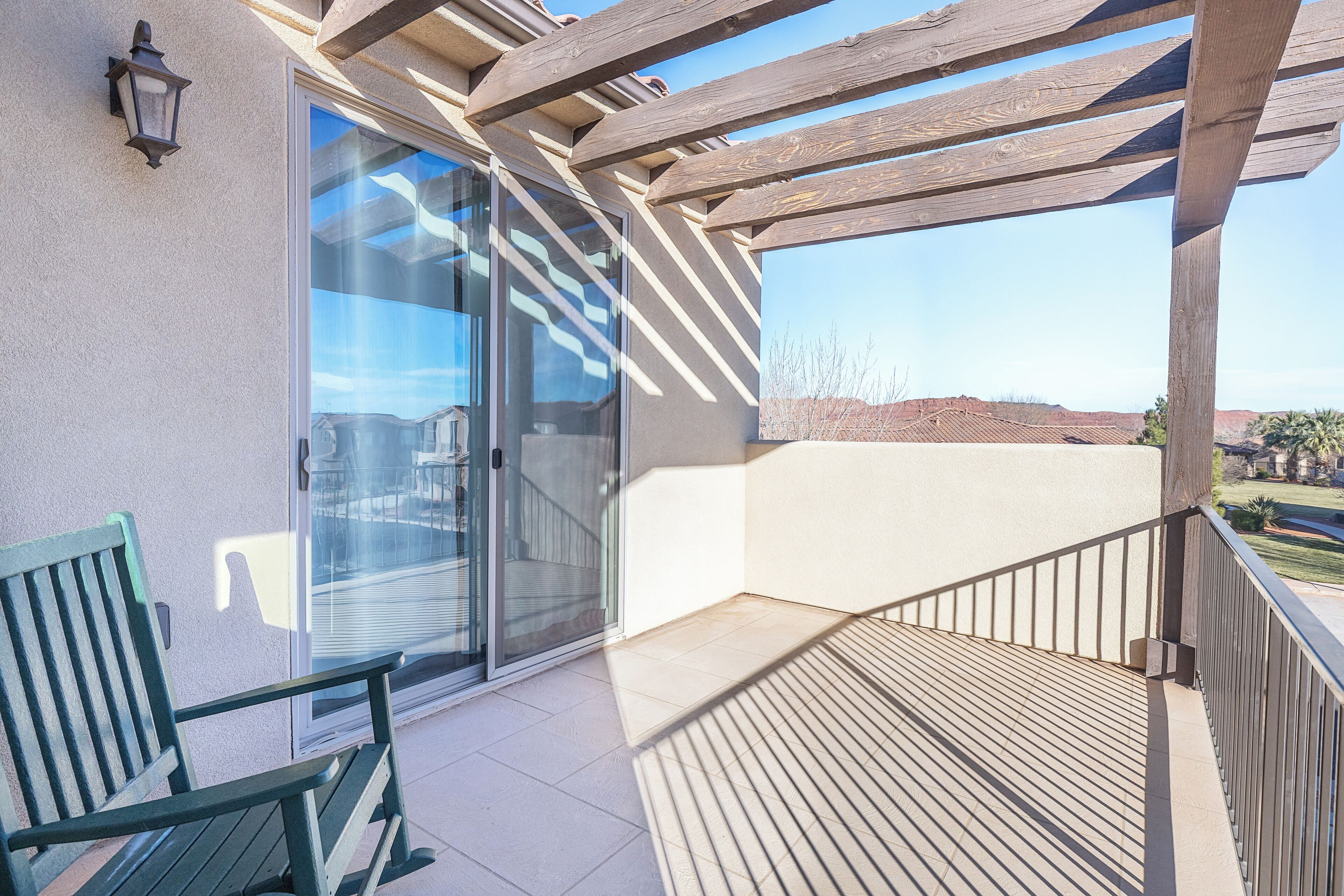 A balcony with a wooden pergola, a bench, and a sliding glass door leading to a patio area.