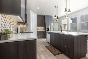 A modern kitchen with dark wood cabinets, a white countertop, and pendant lighting.