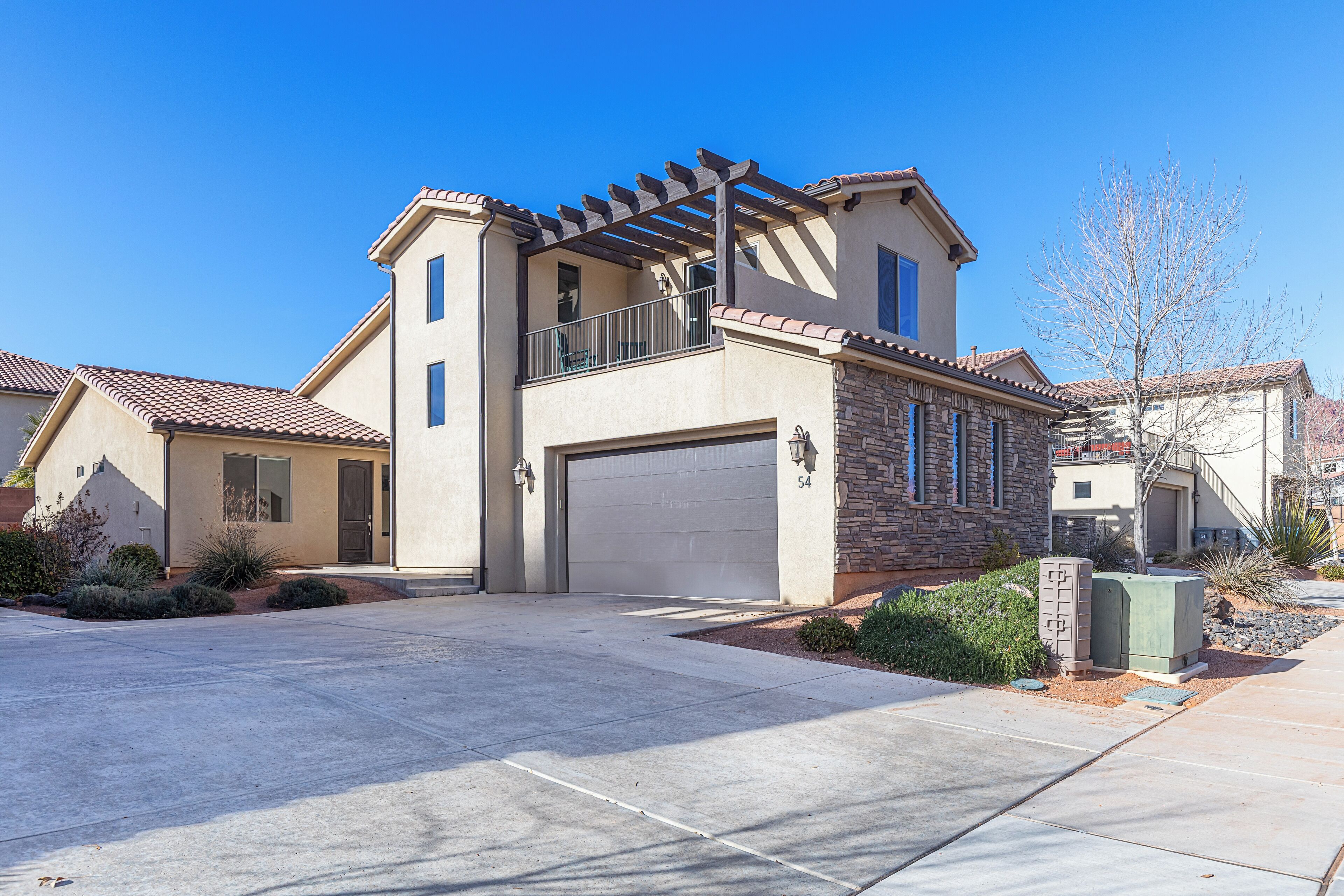 A two-story house with a garage, a balcony with a pergola, and a well-maintained front yard.
