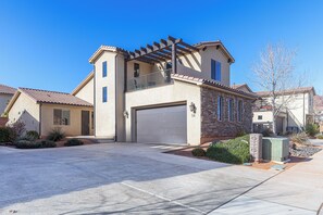 A two-story house with a garage, a balcony with a pergola, and a well-maintained front yard.