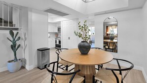 Eine moderne Küche mit weißen Schränken, eine Essecke mit einem runden Holztisch und schwarzen Stühlen sowie eine Deckenleuchte.