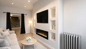 Ein modernes Wohnzimmer mit Kamin, flachbildfernseher an der Wand und Heizkörper.