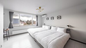 A modern bedroom with a large bed, a window with curtains, a radiator, and a ceiling light fixture.