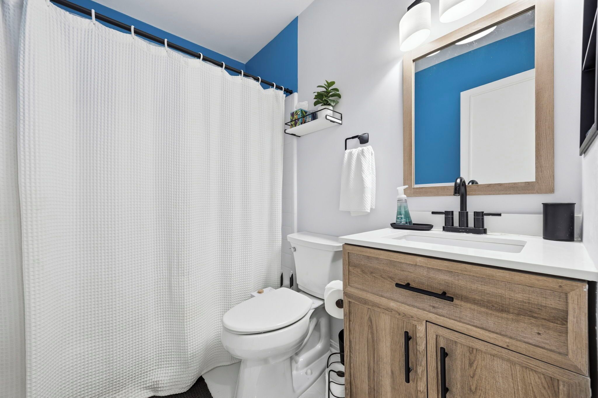 Une salle de bain moderne avec des toilettes blanches, un meuble-lavabo en bois, un miroir et un rideau de douche.
