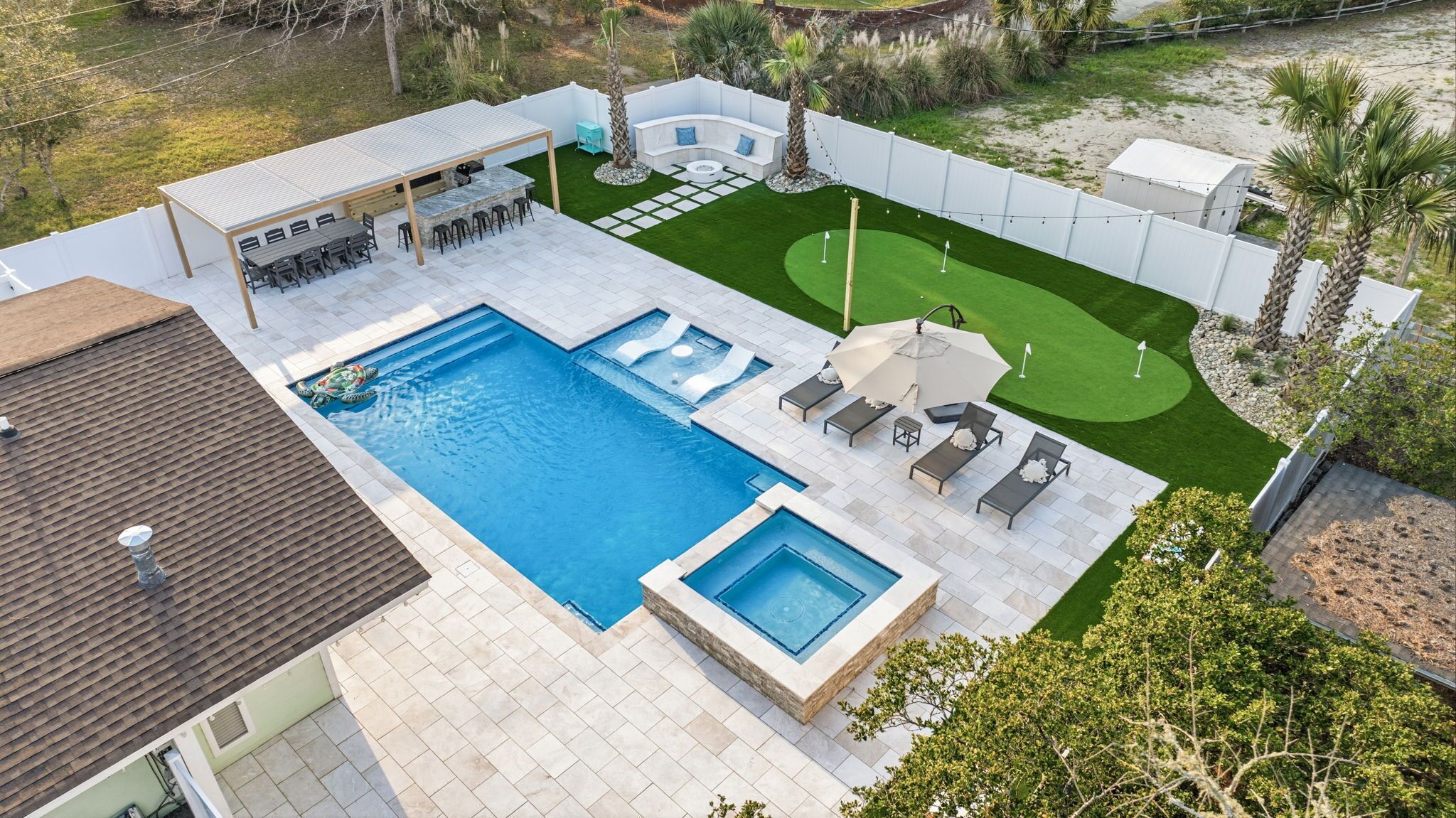 A swimming pool with a hot tub, a seating area with a table and chairs, and a small lawn with a putting green.