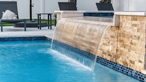 Ein Swimmingpool mit Wasserfall, Liegestühlen und einer Steinmauer.