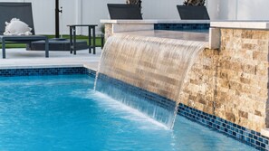 Ein Swimmingpool mit Wasserfall, Liegestühlen und einer Steinmauer.