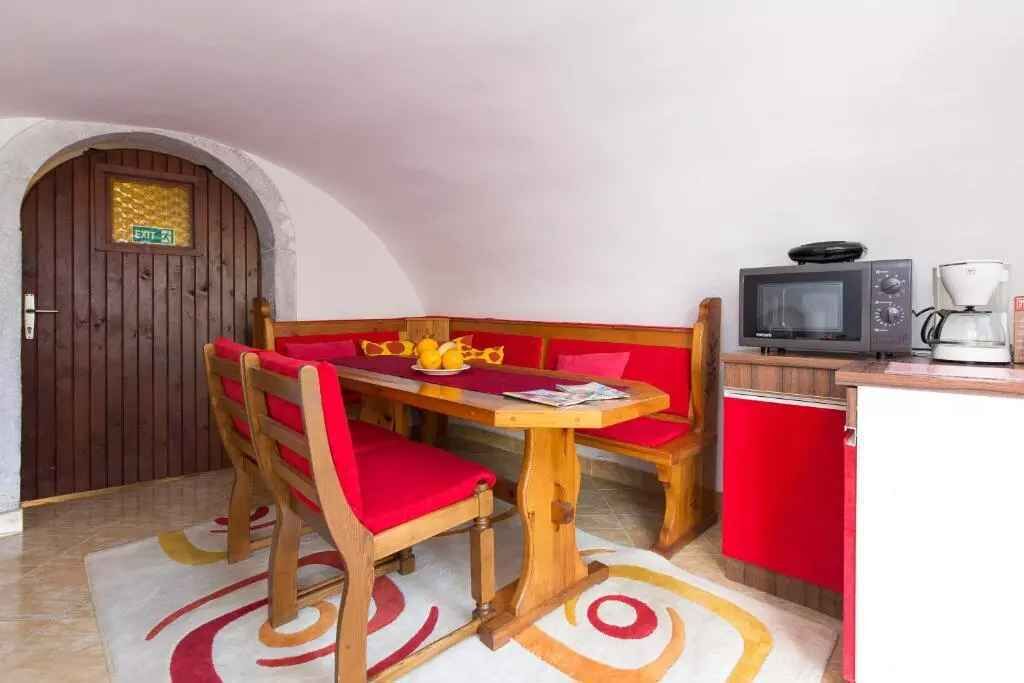 A small kitchenette with a microwave, coffee maker, and a TV. There is a wooden table with red cushions and a bench.