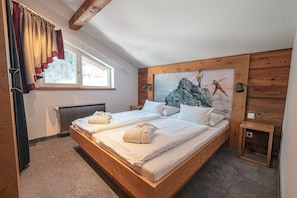 A double bed with white linens and towels, a wooden headboard, a painting of a mountain scene, and a small bedside table with a lamp. - Holiday apartment with wellness area (Brand bei Bludenz)