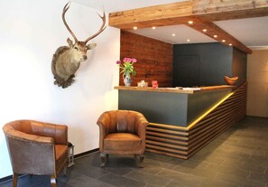 Een receptiegedeelte met een houten receptiebalie, twee leren fauteuils en een opgezette hertenkop aan de muur.