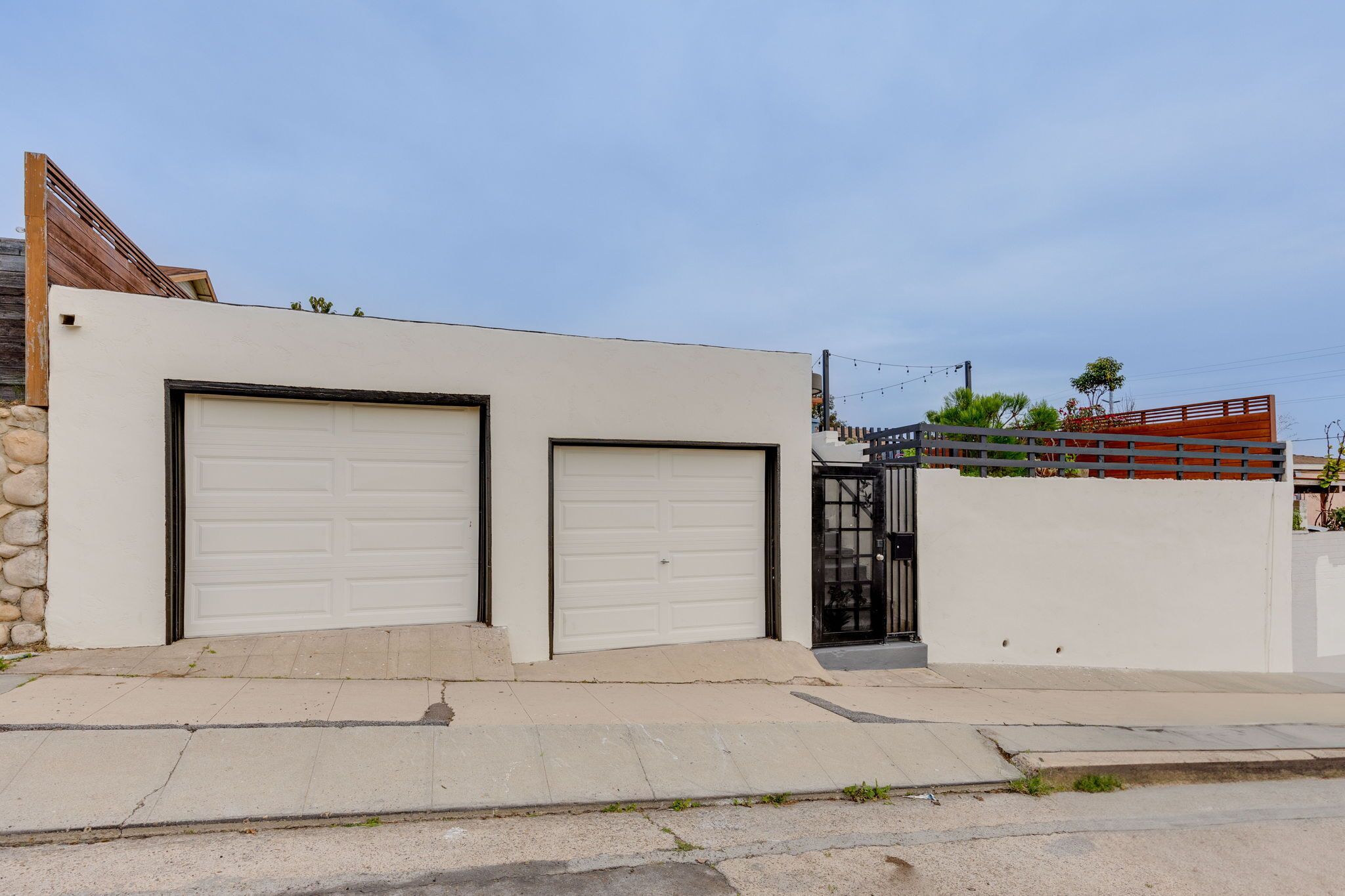 Une maison moderne avec deux portes de garage, un mur en pierre et une clôture en bois.