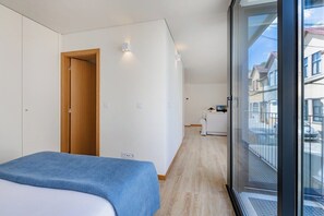 Ein modernes Hotelzimmer mit Bett, einer Holztür, einer kleinen Küchenzeile und einem Balkon mit Blick.