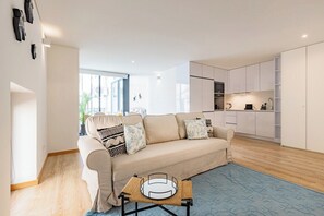 Ein modernes Wohnzimmer mit einer Couch, einem Couchtisch und einer Küchenzeile inklusive Schränken und Geräten.