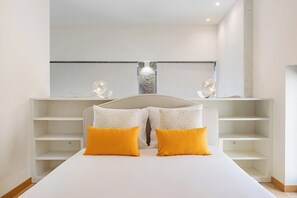 Ein Schlafzimmer mit einem Bett, zwei gelben Kissen, einem weißen Kopfteil und einem großen Spiegel über einer weißen Regaleinheit.