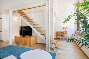 Ein moderner Wohnraum mit einer Holztreppe, einem Fernseher, einem Essbereich und einer großen Pflanze.