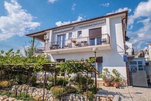 A two-story building with a balcony, outdoor seating, and potted plants. - Holiday apartment with air conditioning (Novi Vinodolski)