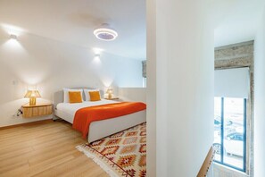 Ein Schlafzimmer mit einem Bett, Nachttischlampen, einem gemusterten Teppich und einem Fenster mit Blick auf parkende Autos.