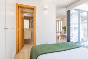 Ein Schlafzimmer mit Bett, grüner Decke, Holztür, Badezimmer mit Waschbecken und einem Balkon mit Blick.