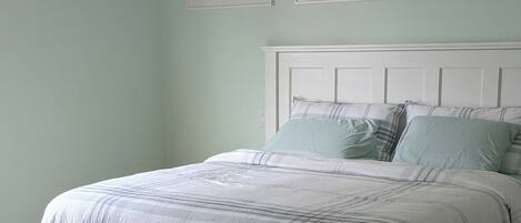 A bedroom with a bed, a wooden floor, and three framed pictures on the wall.