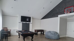 A modern living room with a pool table, a foosball table, a bean bag chair, and a flat-screen TV mounted on the wall. - “Room for Everyone: Seven-Bedroom Lakefront Getaway on Lake Tillery” (Norwood)