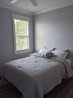 Une chambre à coucher avec un lit, une fenêtre avec des stores et un ventilateur de plafond.