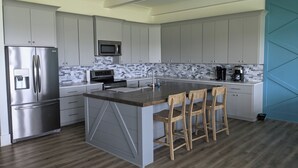 A modern kitchen with a stainless steel refrigerator, a microwave, a coffee maker, and a wooden island with bar stools. - “Room for Everyone: Seven-Bedroom Lakefront Getaway on Lake Tillery” (Norwood)