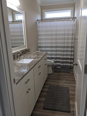 Une petite salle de bain avec un lavabo surmonté d’un plan de travail en granit, des toilettes et un rideau de douche.