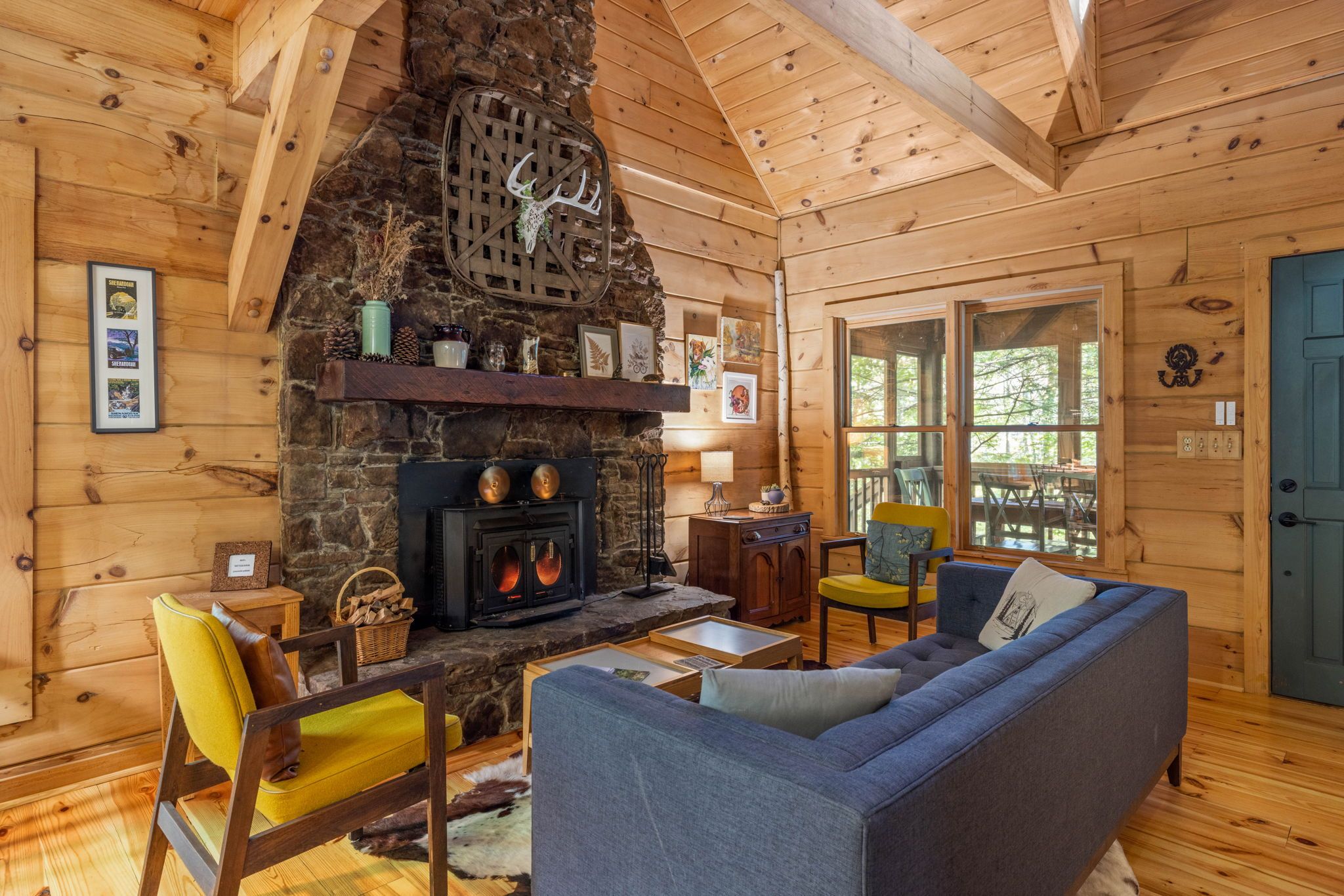 A cozy cabin interior with a stone fireplace, wooden walls, and a comfortable seating area.
