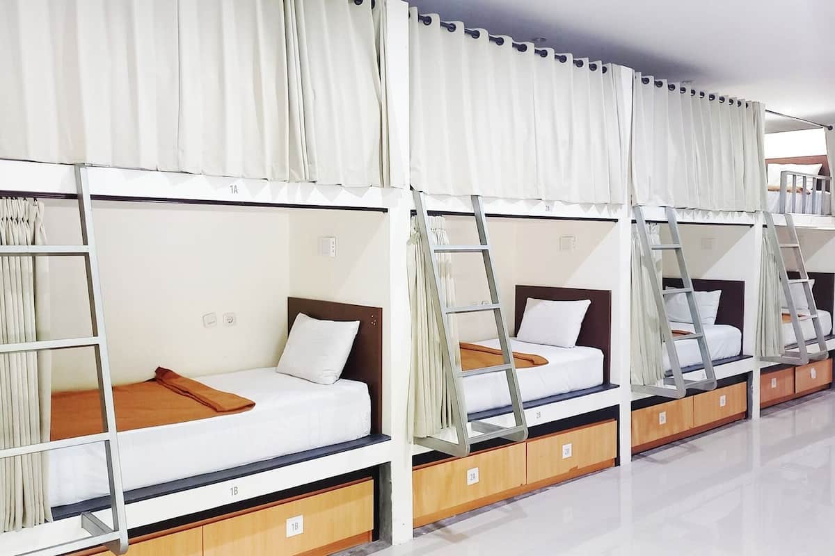 Ein Schlafsaalzimmer mit Stockbetten, jede mit einer Leiter, und einer kleinen Holzkiste unter jedem Bett.