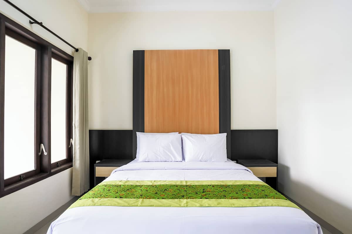 Ein Hotelzimmer mit einem Bett, zwei Nachttischen, einer Kopfteil und einem Fenster mit Vorhängen.